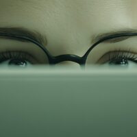 Person peering over laptop screen with focused expression, representing strategic research and buyer question mapping for AEO