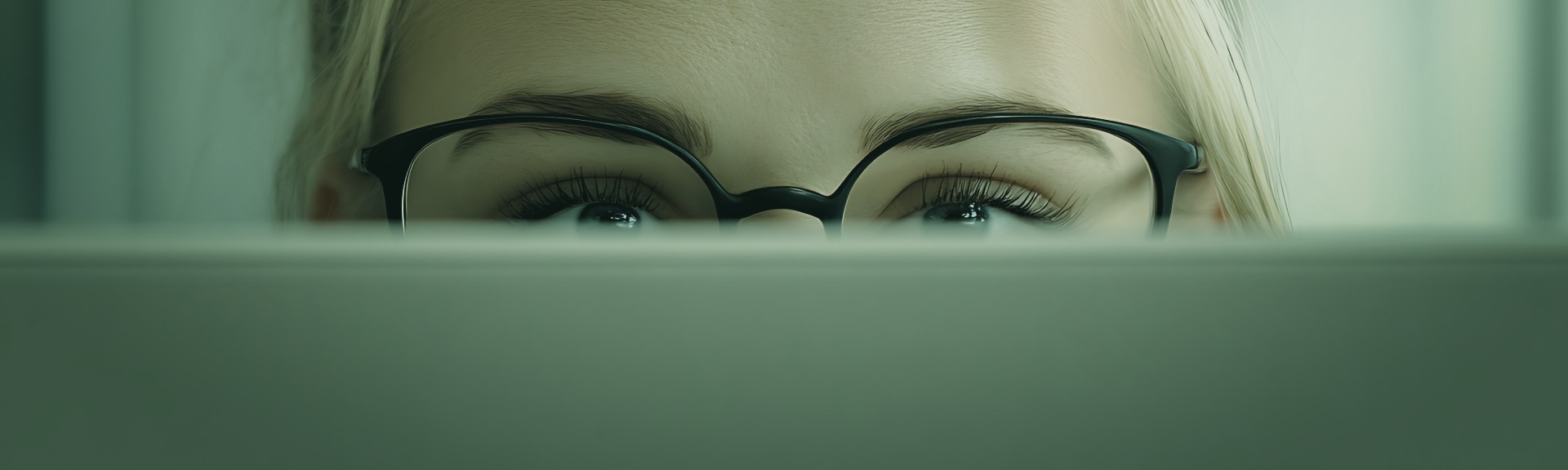 Person peering over laptop screen with focused expression, representing strategic research and buyer question mapping for AEO