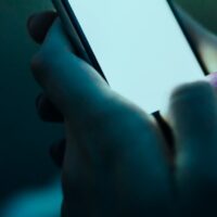 Hand holding a glowing phone screen in dark surroundings, representing buyer search behavior and AI visibility tracking for AEO measurement