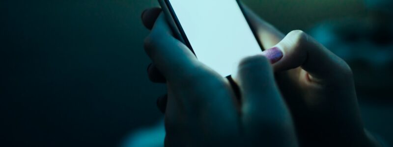 Hand holding a glowing phone screen in dark surroundings, representing buyer search behavior and AI visibility tracking for AEO measurement